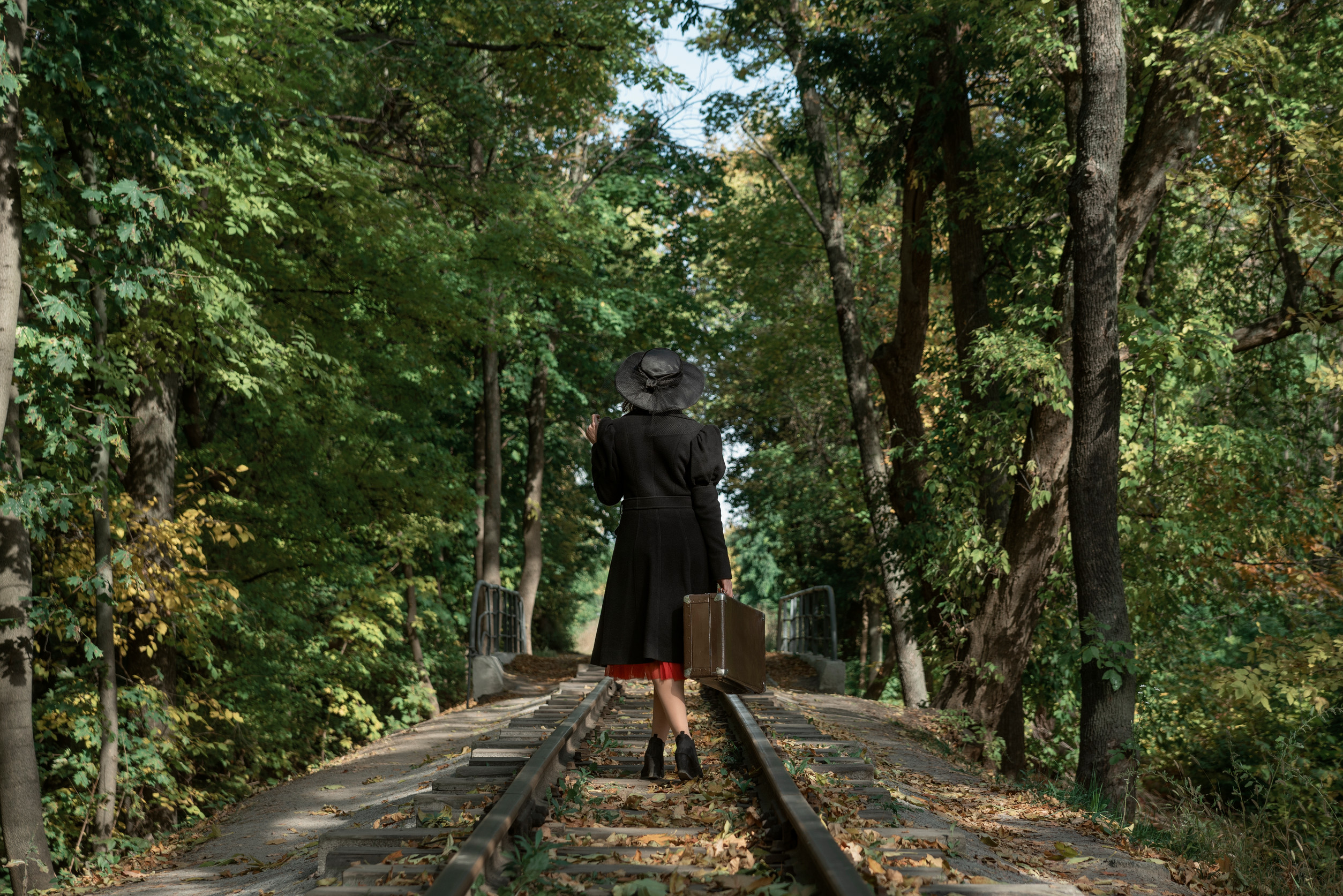 Dirigeante de dos portant une valise sur une voie ferrée en forêt — quitter un poste de direction
